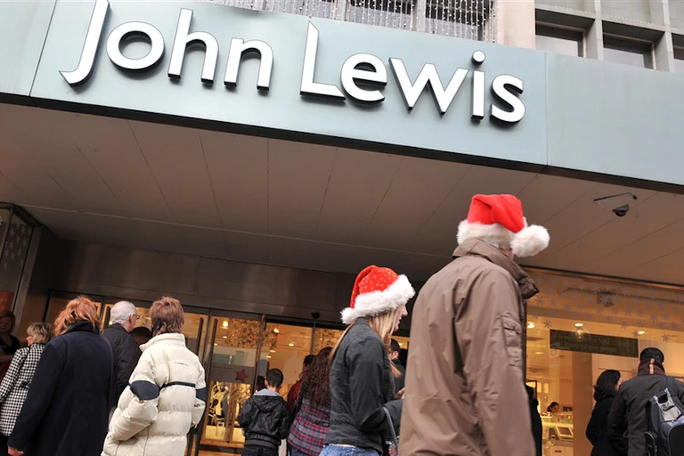 Customers walk past a John Lewis shopfront wearing red Santa hats