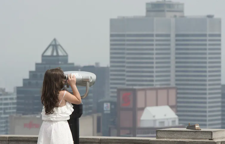 jeune fille regarde Montréal au loin à travers des jumelles