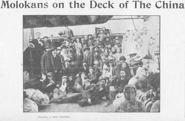 A black and white photograph shows a group of people in relatively formal dress standing together on the deck of a ship.