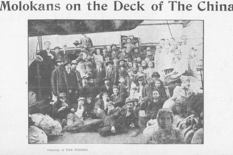 A black and white photograph shows a group of people in relatively formal dress standing together on the deck of a ship.