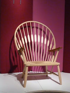 The elegant peacock chair pictured against a rich magenta backdrop. The peacock chair has a wide, round backs that imitates a peacock's plumage