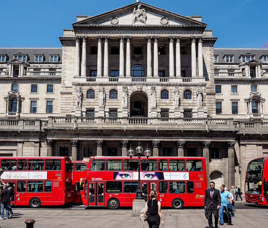 Red buses lined up in front of the Bank of England, people, blue sky.