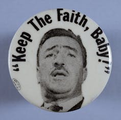 A button with a man's face on it under the motto'Keep The Faith, Baby'.