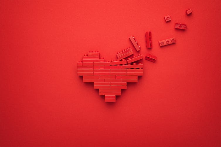 A heart made of lego has some of the pieces flying away.