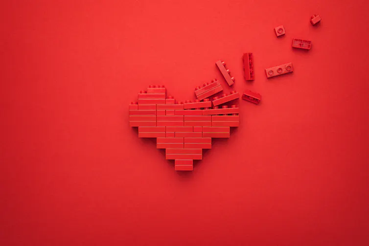 A heart made of lego has some of the pieces flying away.