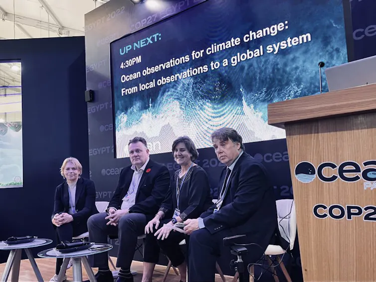 A panel of speakers with a projector screen in the background.
