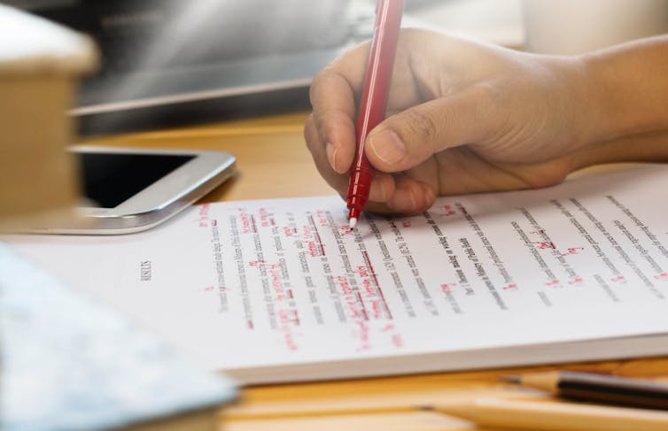 A close-up shot of someone holding a red pen and revising a text.