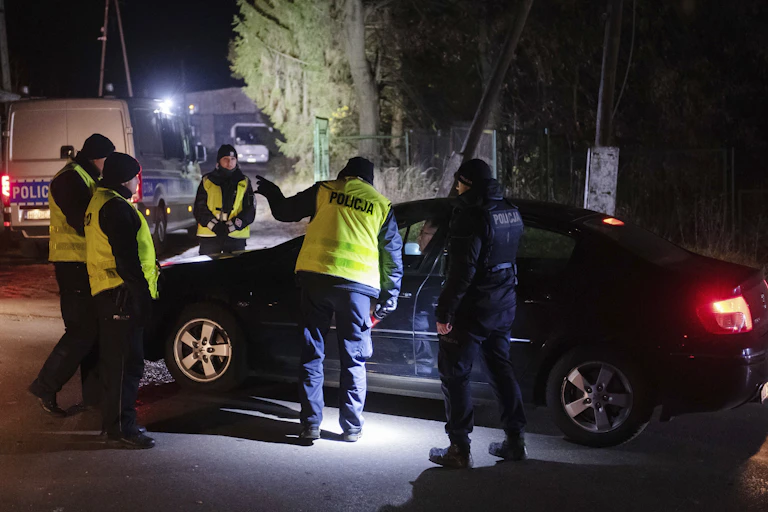 Polish police in fluorescent jackets stand by a car.