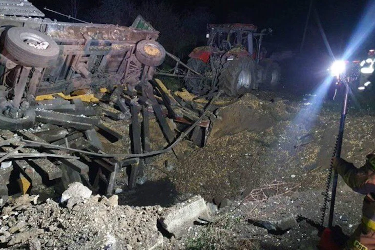 A night photo of a large hole from an explosion, with a toppled trailer.