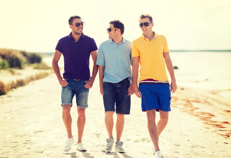 Three young men walking together on a beach.