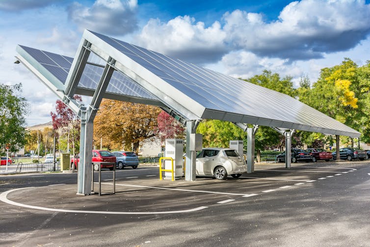 Two solar panel arrays suspended at an angle over a parked car.