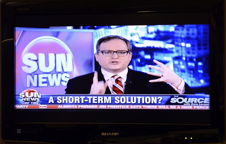 A television screen shows a dark-haired man speaking with a large Sun News logo behind him.