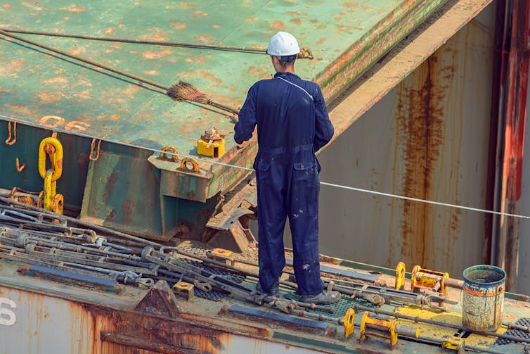 A longshore worker sweeping long rods, which are used to secure containers on a ship, with a broom