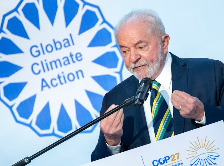 A bearded man at a lectern in front of a sign reading 'Global Climate Action.'