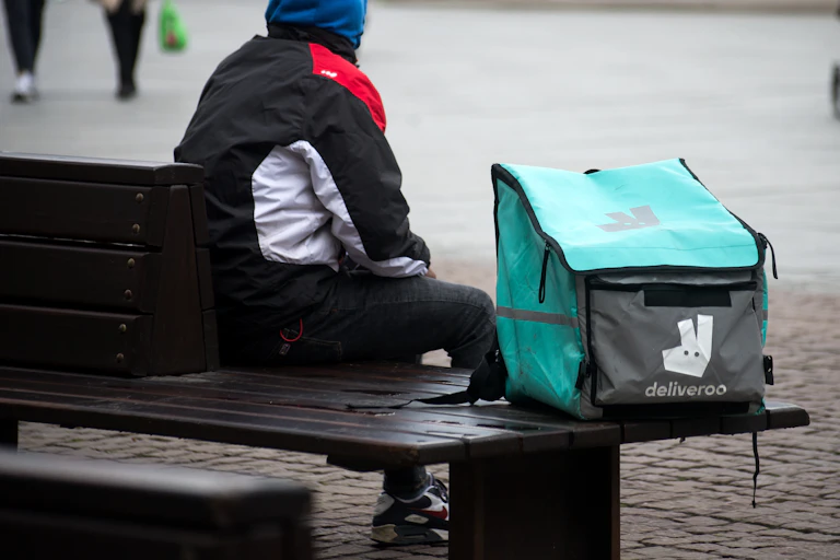 Deliveroo worker sitting on street bench.