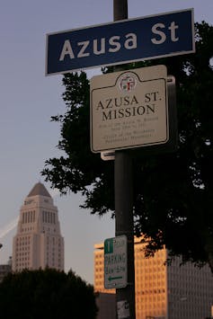 A skyscraper stands in the distance behind a street sign reading 'Azusa St,' with an informational sign about the Asuza Street Mission.