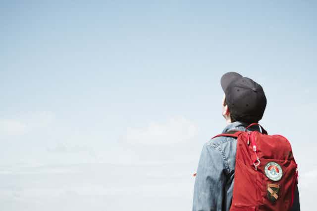 Young man with backpack, looks up at blue sky
