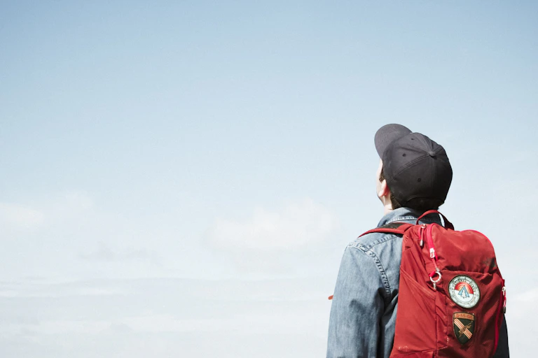 Young man with backpack, looks up at blue sky