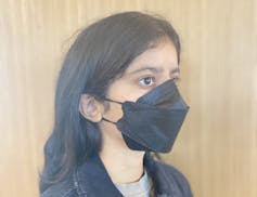 A young woman wearing a black face mask with ear loops