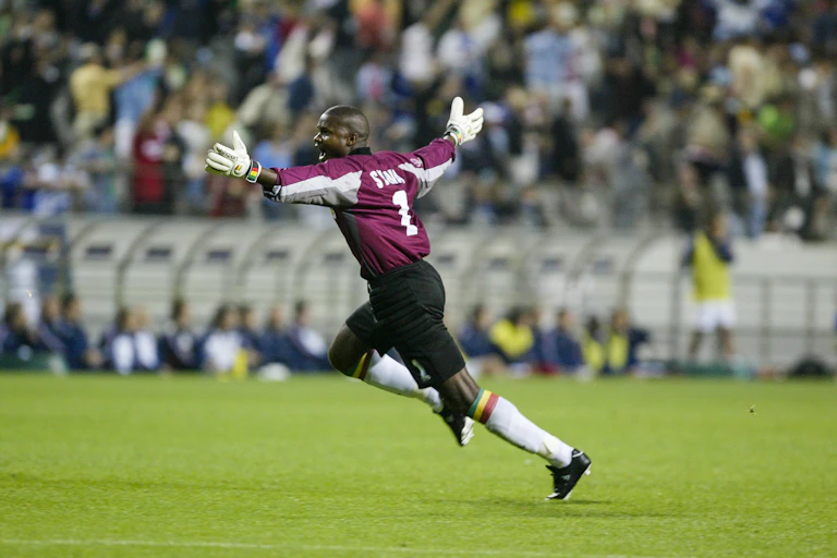 A footballer wearing gloves runs across the field, arms outstretched.
