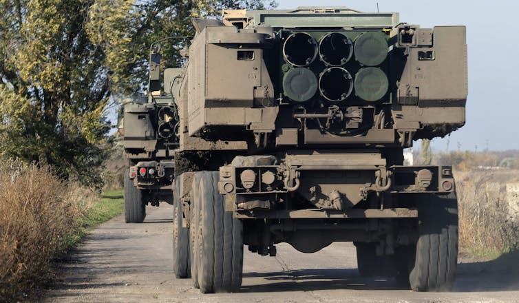 Military vehicles with in-built rocket launchers driving down country road.