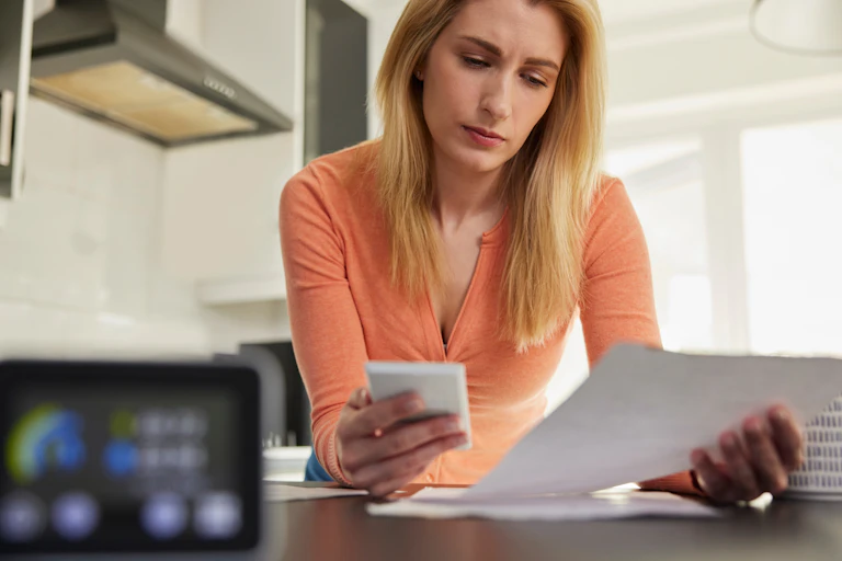 A woman in an orange top looking at her bills with a calculator in her hand.
