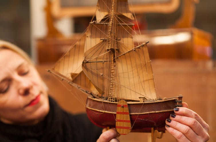A woman holds a vintage boat figurine and looks at it intently