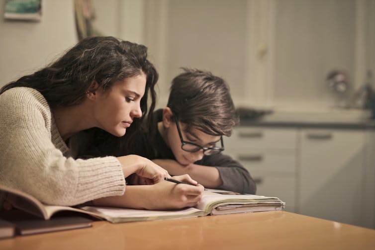 A mother next to a teen looking at homework.