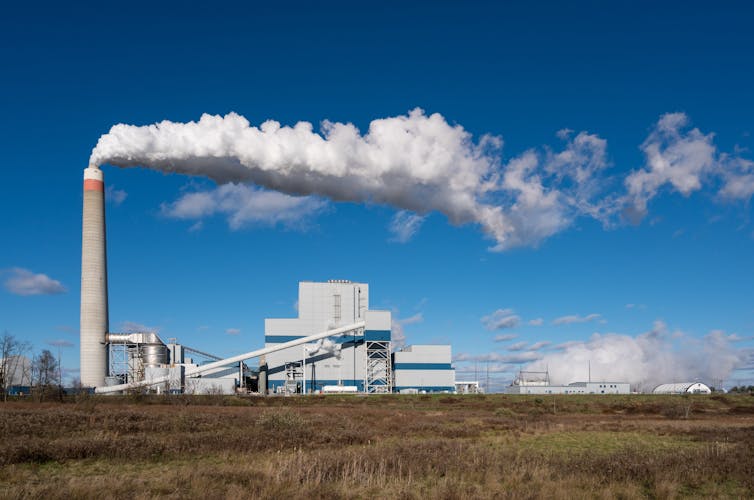 A power plant chimney bellows white smoke on a wide plain.