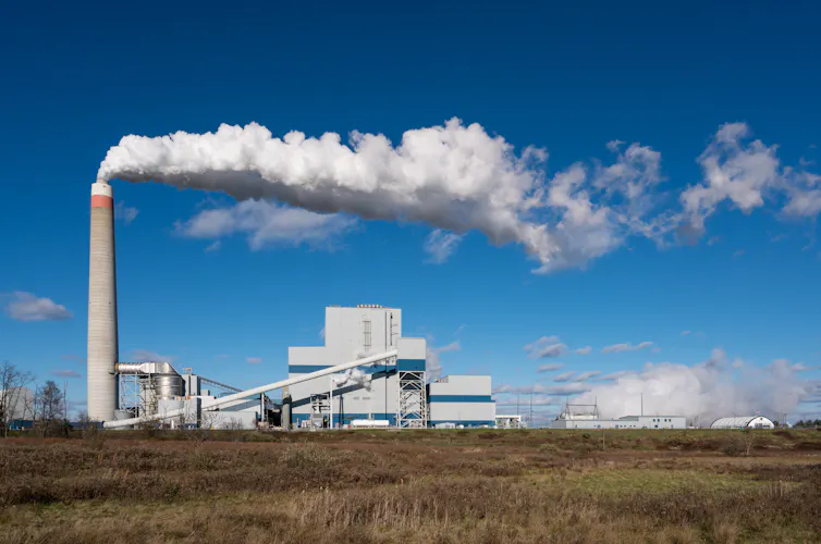 A power plant chimney bellows white smoke on a wide plain.