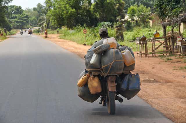 A man on a motorcycle laden with bottles of fuel.