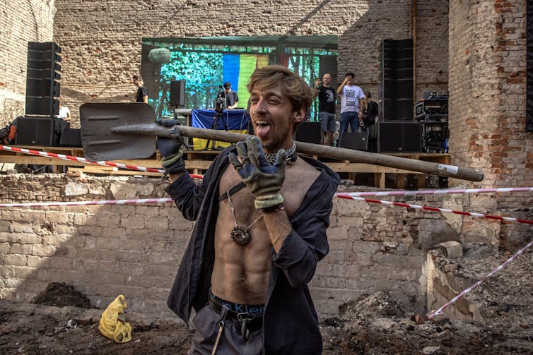 A young Ukrainian man with a shovel dances as he helps clean up a bomb site.
