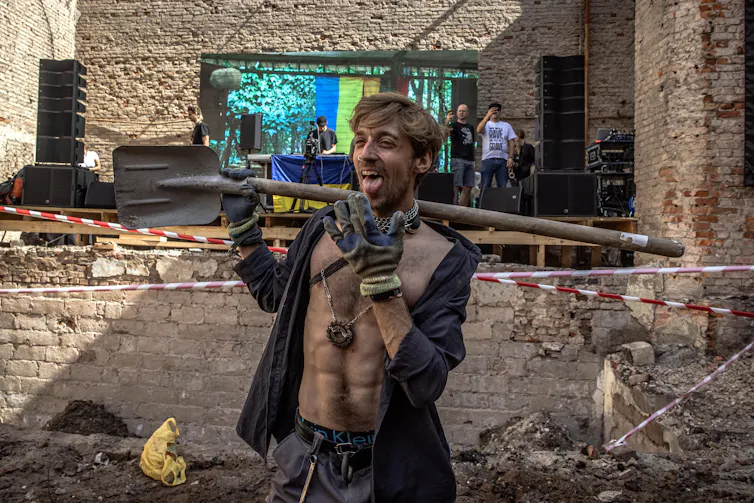 A young Ukrainian man with a shovel dances as he helps clean up a bomb site.