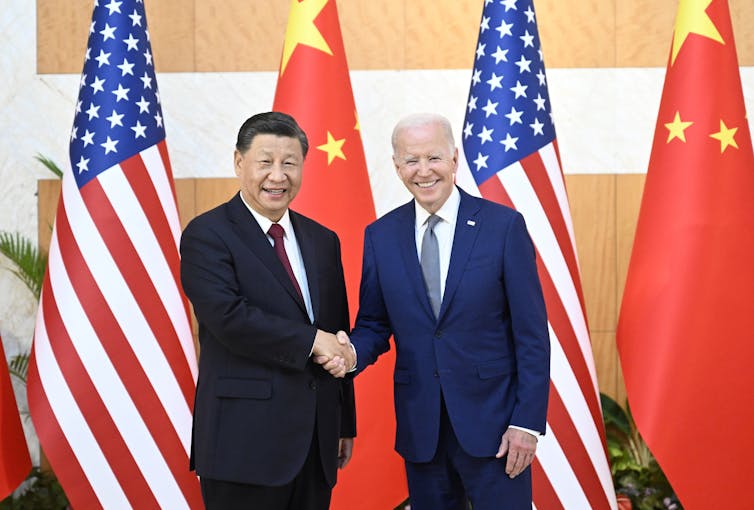 Chinese president Xi Jinping and US president Joe Biden shake hands in front of their countries' flags.