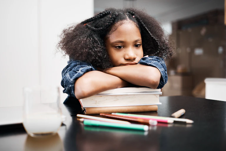 A girl with her arms crossed over a pile of books, resting her chin on her arms