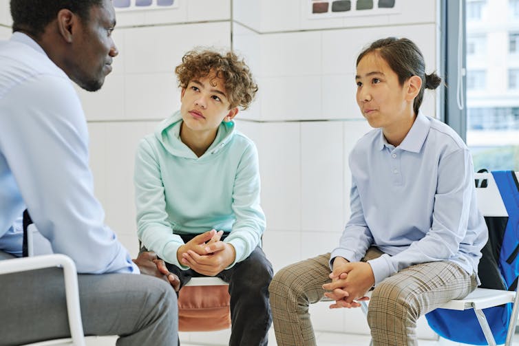 Two teen boys listening to an adult; all three are sitting in chairs facing each other,