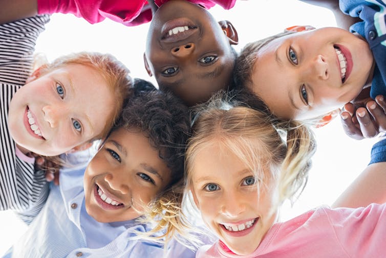 Closeup faces of happy children embracing each other and smiling, photographed from below