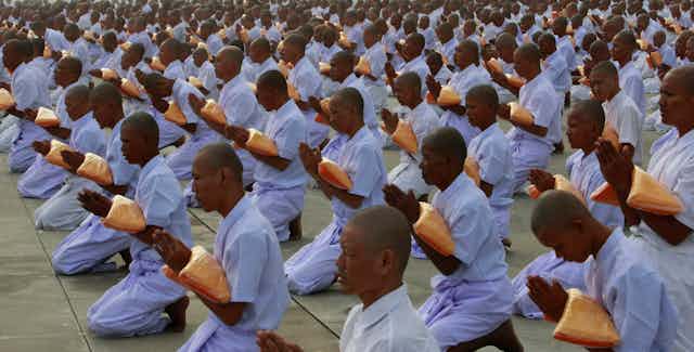 Monks dressed in white garments holding folded saffron robs and chanting prayers