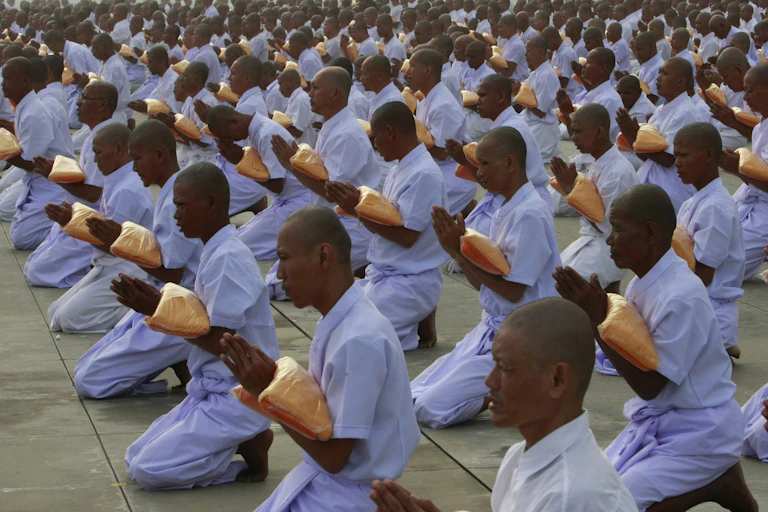 Monks dressed in white garments holding folded saffron robs and chanting prayers
