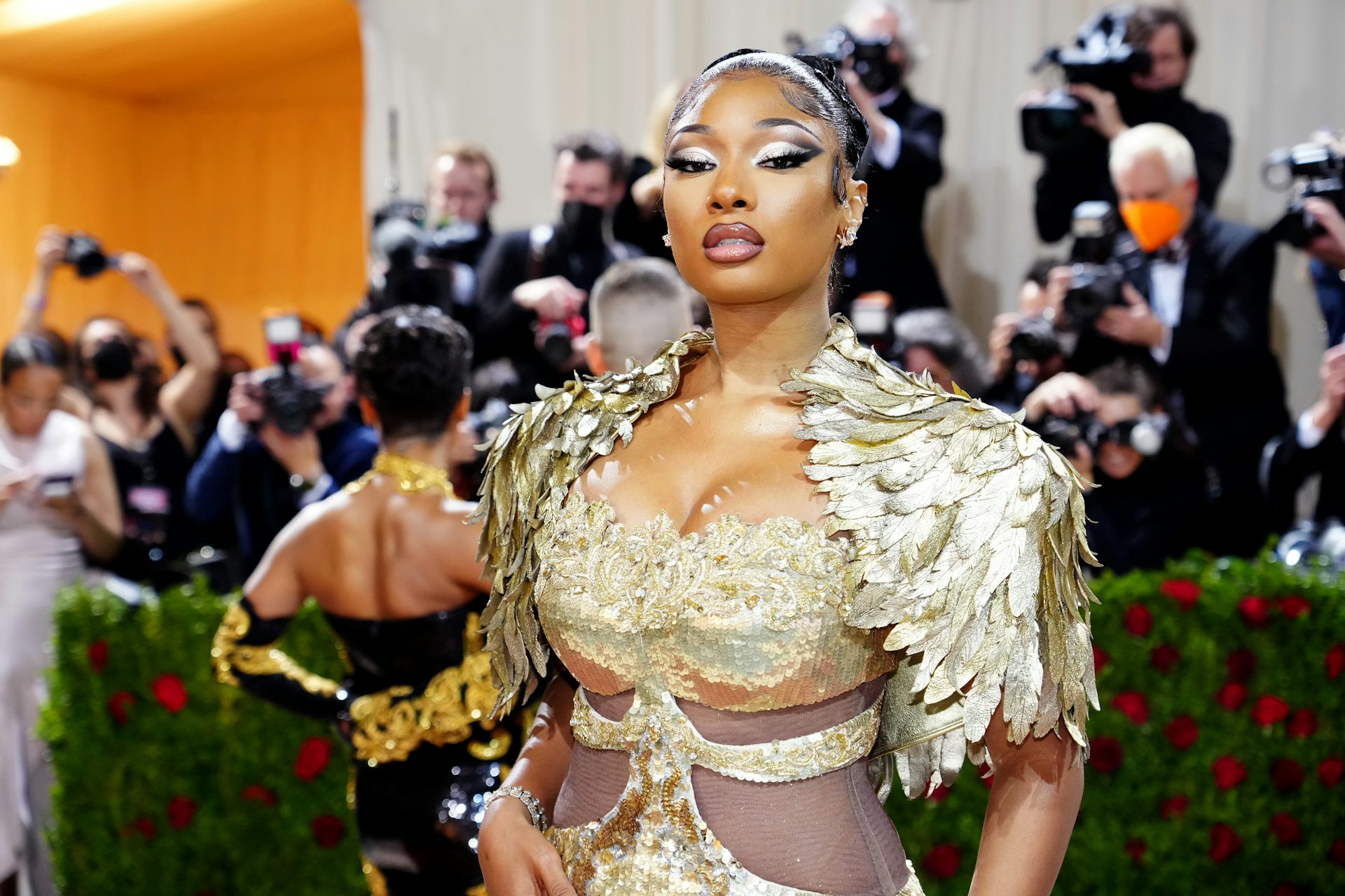 A Black woman dressed in a fancy gold gown poses for photographers.