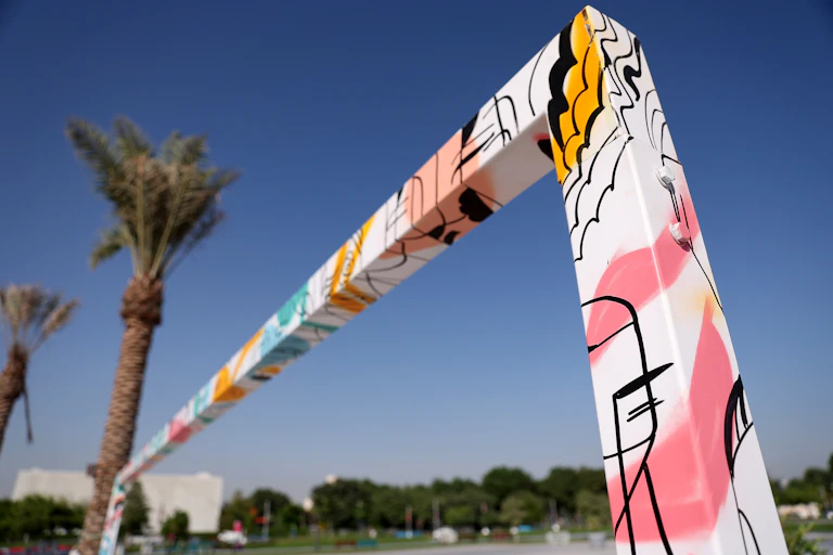 Goalposts painted pink and yellow stand in front of a palm tree.