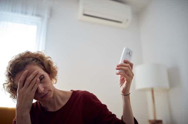 woman feeling the heat holds up a remote to adjust the air conditioner