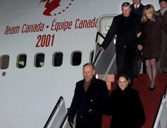 A man and a dark-haired woman disembark from a plane that says Team Canada in both official languages.