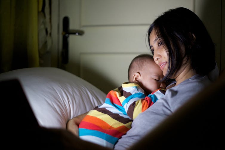 A woman looks at a screen while holding a baby.