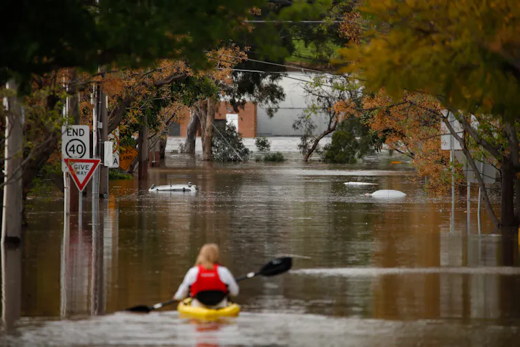 a woman in a canoe, travelling a flooded street in Maribyrnong, Melbourne