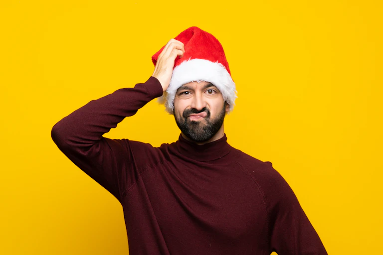 Man with Christmas hat over isolated yellow background with an expression of frustration and not understanding