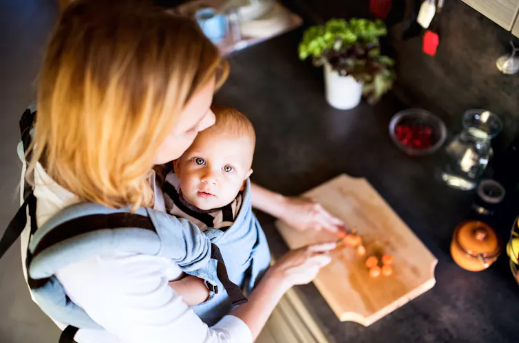Woman with baby in sling chops vegetables.