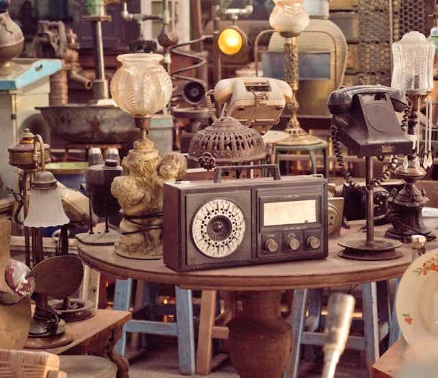 A cluttered vintage shop with old heirlooms like lamps, radios and telephones