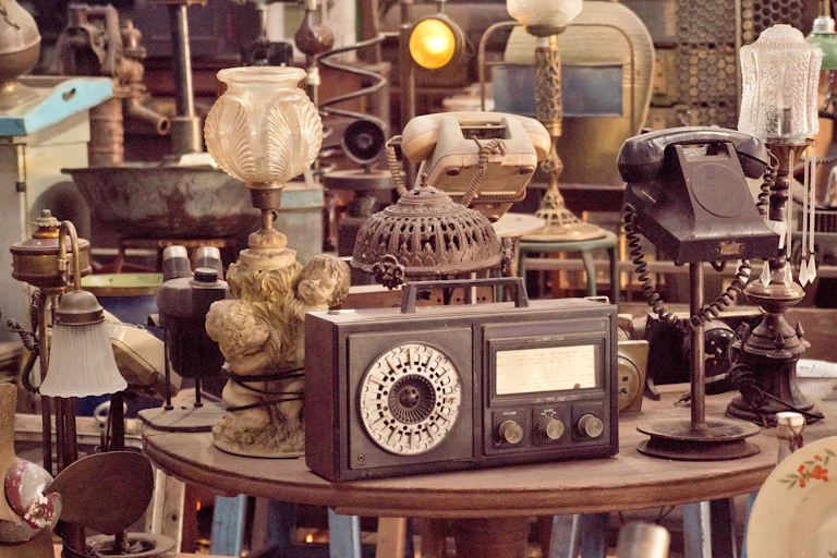 A cluttered vintage shop with old heirlooms like lamps, radios and telephones