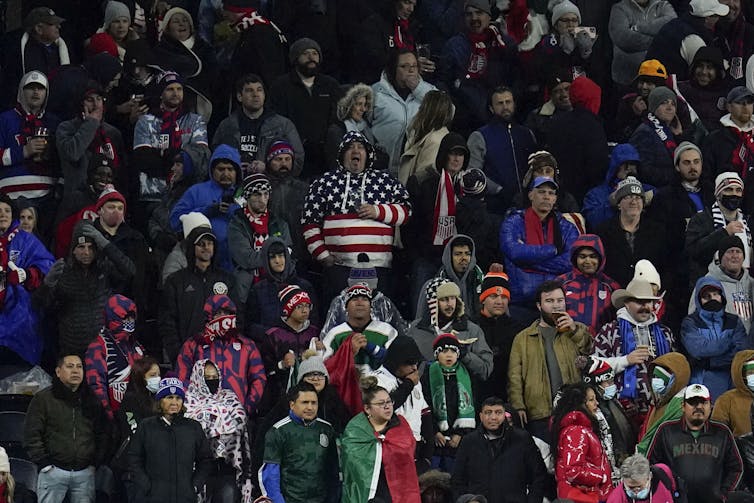 A man in a 'stars and stripes' hoodie is surrounded by other supporters.